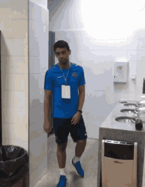 a man in a blue shirt with a lanyard around his neck walks through a bathroom
