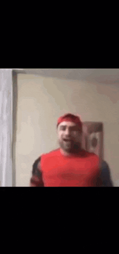 a man in a red shirt and red hat is standing in front of a window .