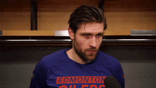 a man wearing a blue edmonton oilers shirt talks into a microphone