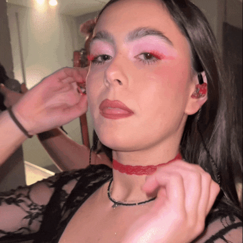 a woman wearing a choker and red eye shadow looks at herself in the mirror