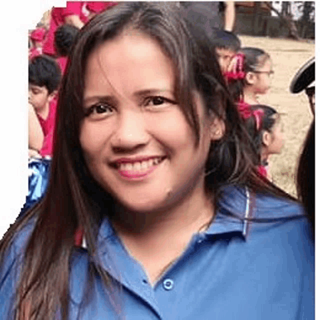 a woman in a blue shirt is smiling for the camera while standing in front of a group of children .