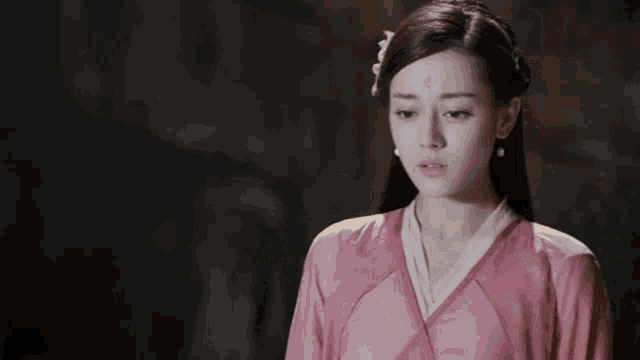 a woman in a pink dress with a flower on her forehead is standing in a dark room .