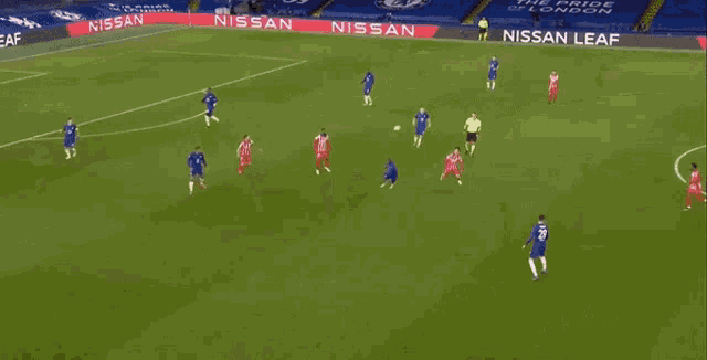 a group of soccer players are playing a game on a soccer field with a nissan ad in the background .