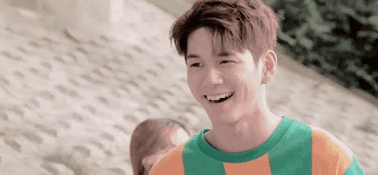 a young man in a green and orange striped shirt is smiling and looking at the camera .