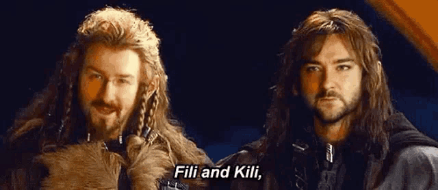 two men with long hair and beards are standing next to each other and talking to each other .