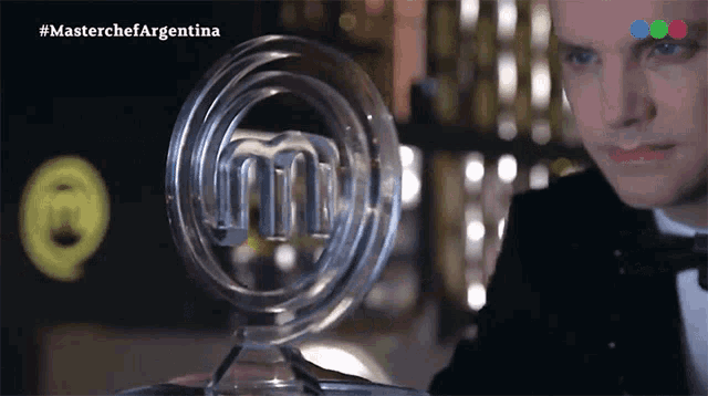 a man in a tuxedo is holding a glass trophy with the master chef logo on it