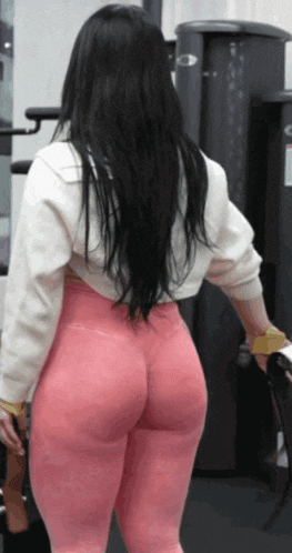a woman wearing pink leggings and a white sweater is standing in a gym