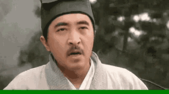 a man with a mustache wearing a hat and a white shirt is making a funny face .