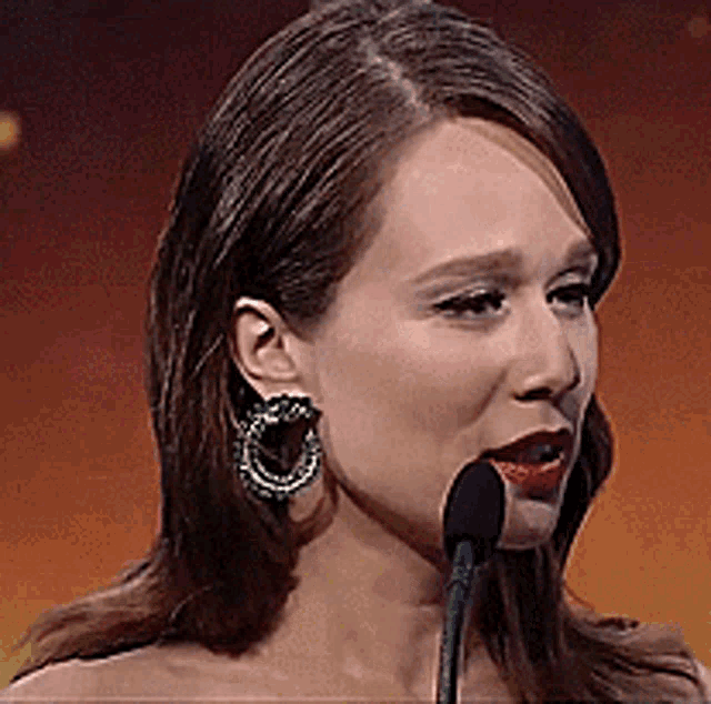 a woman speaking into a microphone wearing earrings