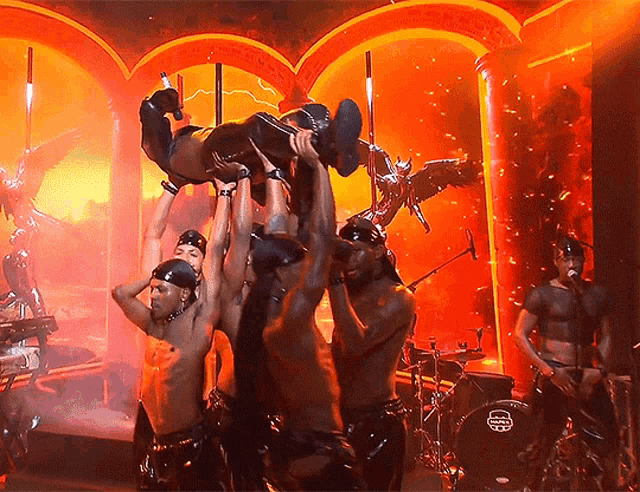 a group of men are holding a woman up in the air in front of a sabian drum set