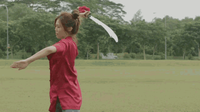 a woman in a red jacket is holding a sword in a field