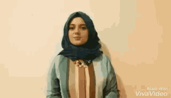 a woman wearing a hijab is standing in front of a wall and singing .