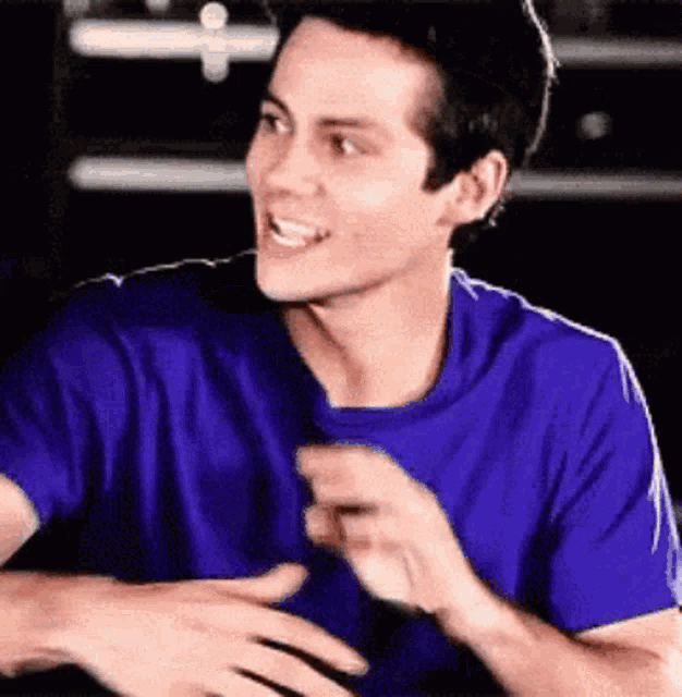 a man in a blue shirt is smiling with his hands on his chest