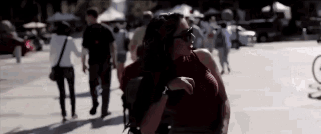 a woman in a red top and sunglasses is standing in front of a crowd of people .