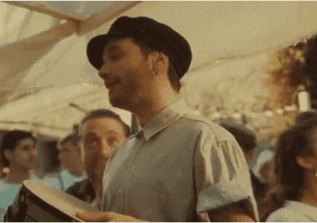 a man in a hat is playing a drum in front of a crowd .