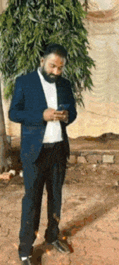 a man in a suit and hat is standing on a sidewalk looking at his phone .