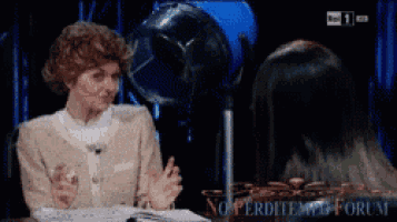 a woman is sitting at a table talking to another woman in front of a fan with the words " no perditem forum " on the screen