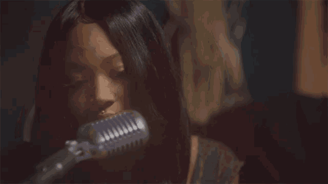 a close up of a woman singing into a microphone with her mouth open