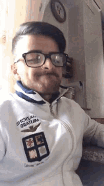 a man with glasses and a beard is wearing a white jacket .