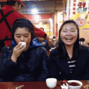 two women are sitting at a table in a restaurant laughing and eating food
