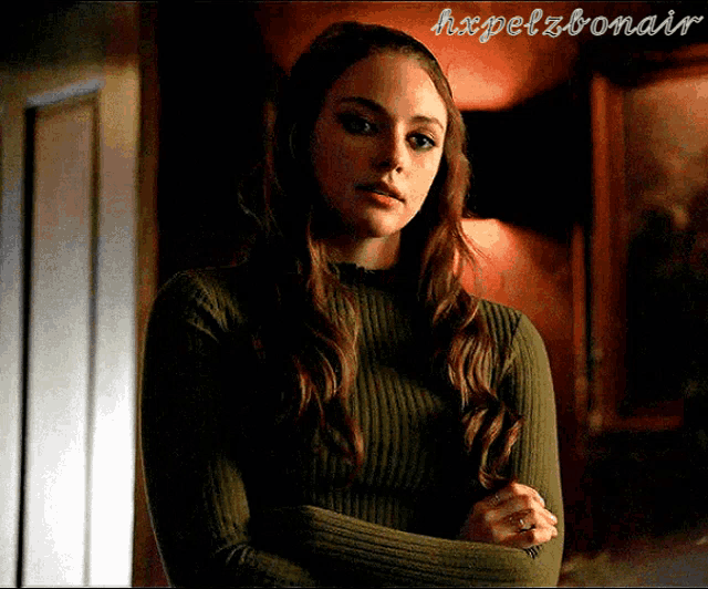 a woman in a green sweater is standing with her arms crossed in a dark room