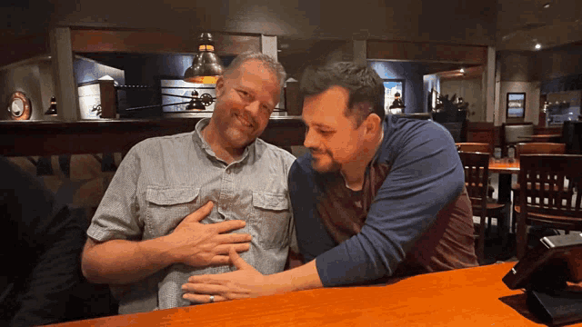 two men are sitting at a table and one has his hand on the other 's chest