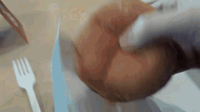 a close up of a person holding a doughnut with a knife and fork in the background