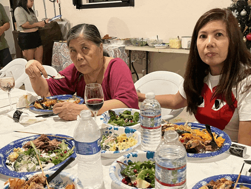 two women are sitting at a table with plates of food and water bottles