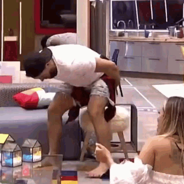 a man is carrying another man on his back in a living room while a woman watches .