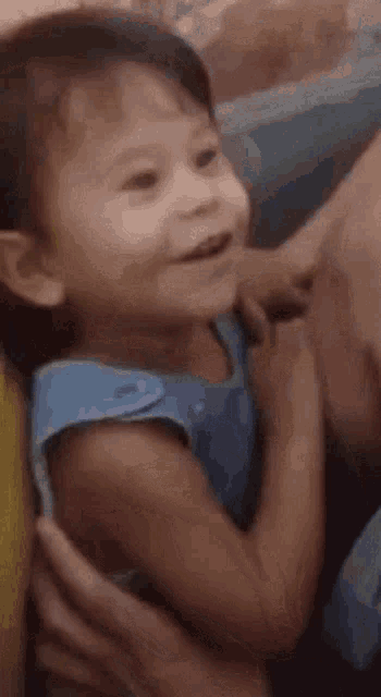 a little girl in a blue shirt is being held by a person .