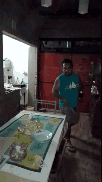 a man in a blue shirt with a sailboat on it stands in a kitchen