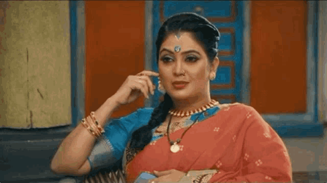 a woman in a red saree and blue blouse is sitting on a chair .