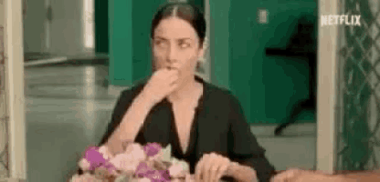 a woman is sitting at a table with a vase of flowers and eating something .