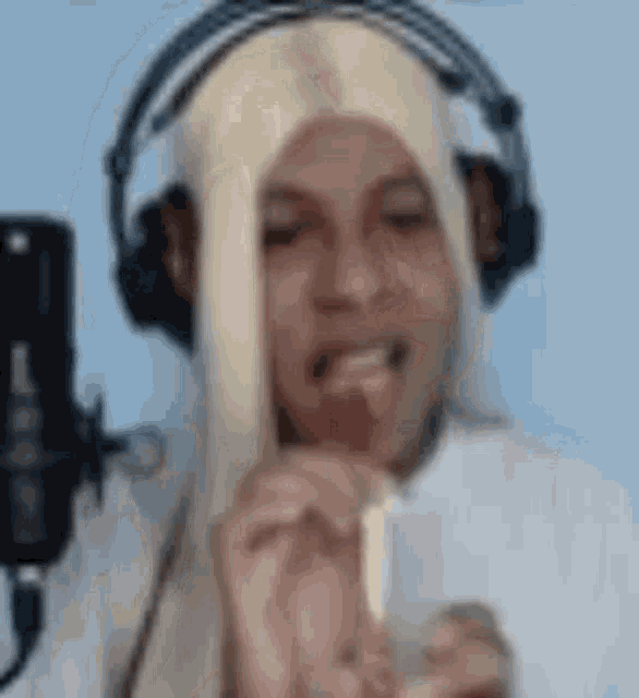 a man in a wig is eating a lollipop in front of a microphone .