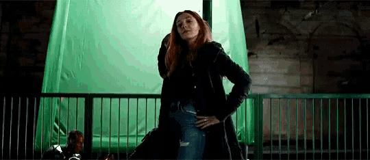 a woman is standing on a balcony with her hands on her hips and a green screen behind her .