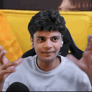 a young man in a white sweater is sitting in a chair with his hands outstretched .