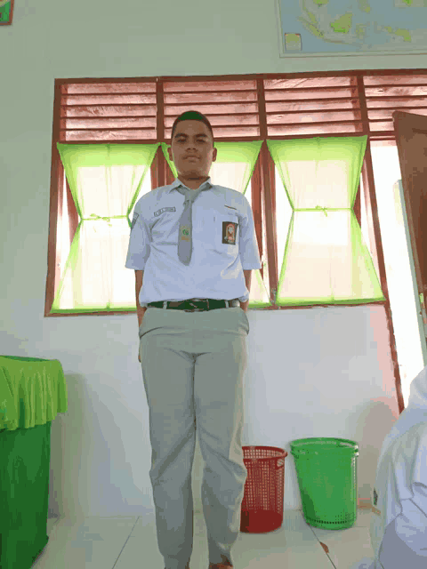 a young man wearing a white shirt and tie with the name muhammad on it stands in front of a window