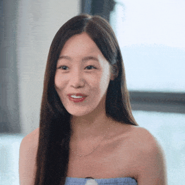 a woman wearing a blue strapless top and a necklace smiles for the camera