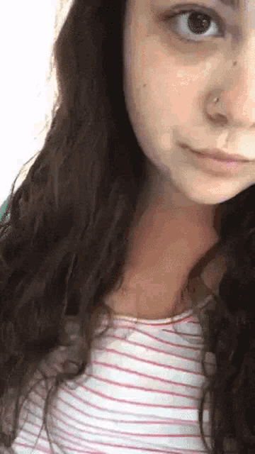 a close up of a woman 's face with a nose ring and a striped shirt