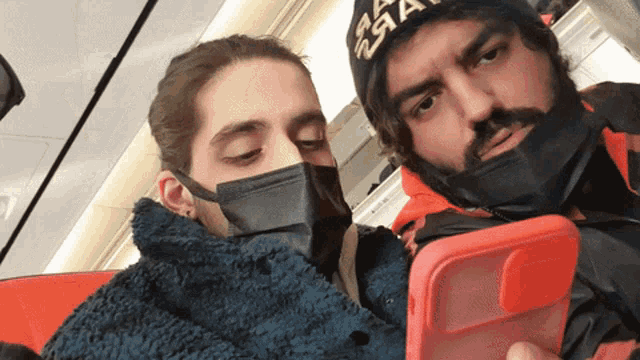 a man and a woman wearing masks are looking at their phones