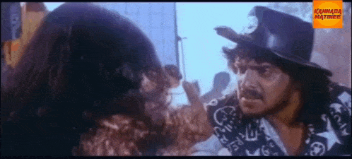 a man in a top hat is talking to another man in a kannada matinee movie .