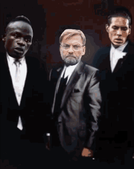 a man with glasses and a beard stands between two men in suits