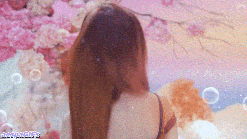 a woman with long hair stands in front of a wall of pink flowers and bubbles