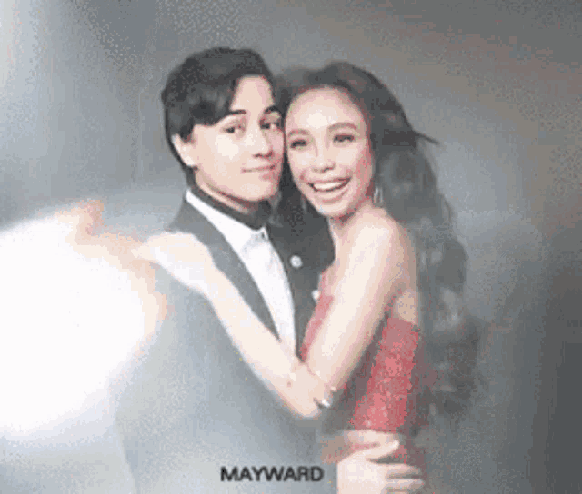 a man in a suit and a woman in a red dress are hugging each other .