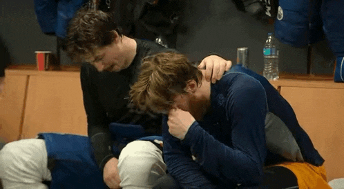 two men are sitting next to each other in a locker room and one of them is holding the other 's head .