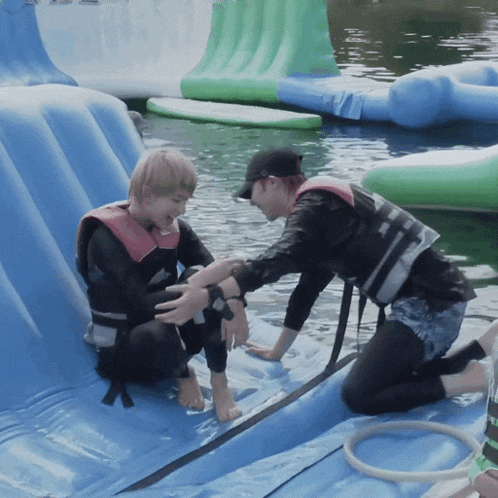 a man in a life jacket helps another man in a life jacket on a water slide