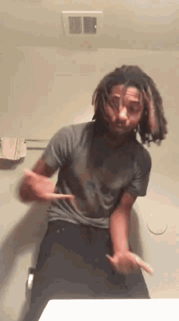 a man with dreadlocks is dancing in front of a mirror in a bathroom