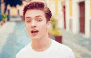a young man wearing a white t-shirt and a necklace looks at the camera