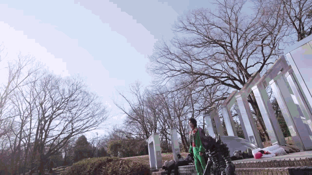a man in a green jacket stands in front of a building with trees in the background