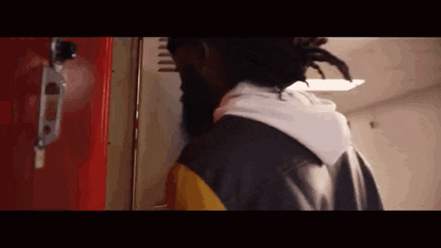 a man with dreadlocks is standing in front of a red locker in a hallway .